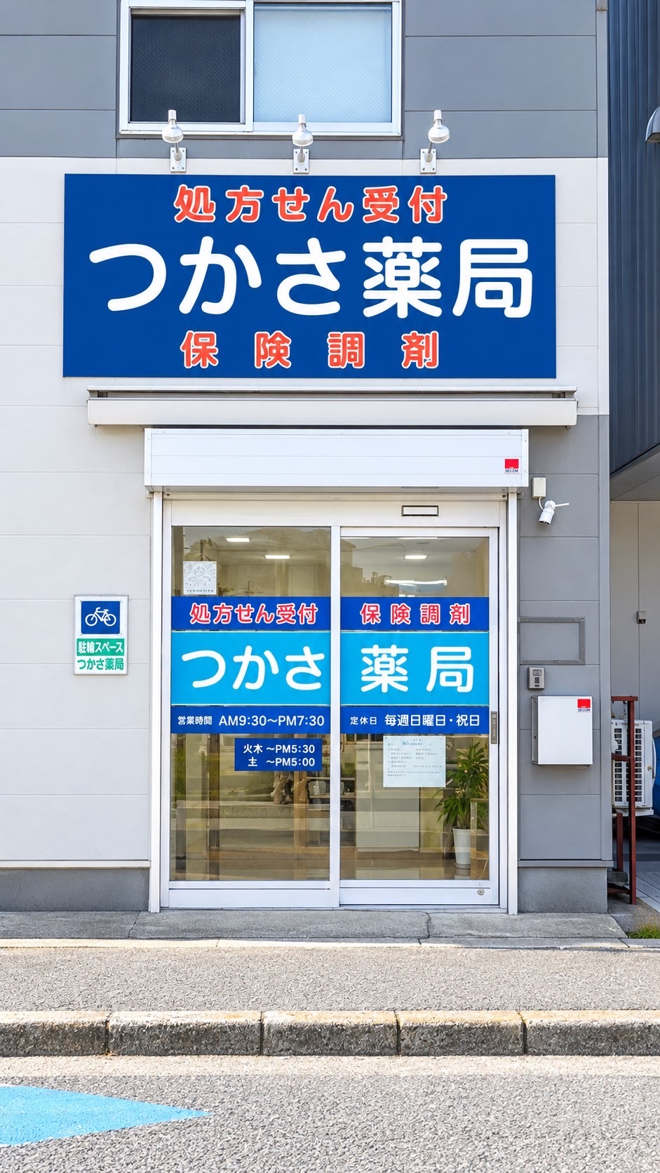 つかさ薬局の外観。「処方せん受付 つかさ薬局 保険調剤」と書かれた青い看板と、水色の入口